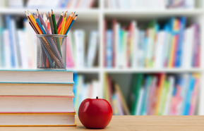An apple, pens and books on a desk.