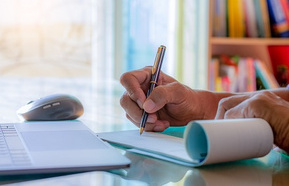 Business man hand writing and signing cheque book with laptop computer on the wooden table at modern home office