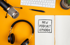 top view of text NEW PODCAST EPISODE on notepad on desk with microphone, computer keyboard and headphones, podcasting concept