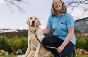 Image of guide dog sitting and being petted by Guide Dogs staff member 