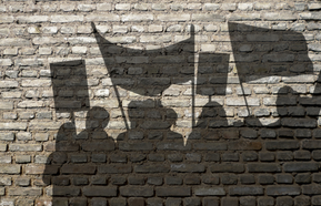 Demonstration: Silhouette of protesters with banners against a grey brick wall
