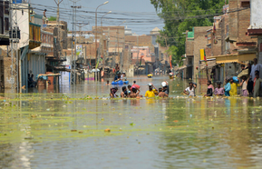 Flooded houses with people walking through the water in Pakistan.
