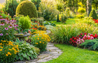A vibrant garden with a winding stone path, diverse blooming flowers, lush green shrubs, and manicured lawn