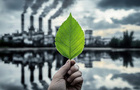 green leaf held in front of polluting factory