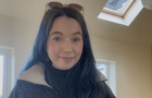 A white girl with dark brown hair and sunglasses on her head.