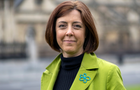 This is a headshot of Kate looking to camera, with a lime green blazer wearing the charity badge.